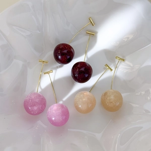 Chic resin cherry drop earrings in red, pink, and champagne gold on a white ceramic tray