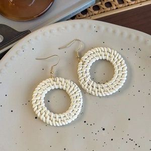 Close-up of bohemian woven rattan hoop earrings with gold hooks on a ceramic plate
