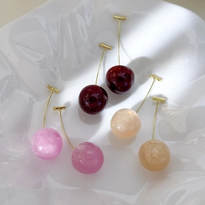 Detail of glitter resin cherry earrings in pink and red on a wavy white plate