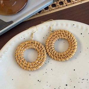 Detail view of round woven rattan earrings on a white ceramic tray with bohemian vibes