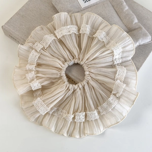 Close-up of beige chiffon scrunchie with lace trim on a minimalist fabric background