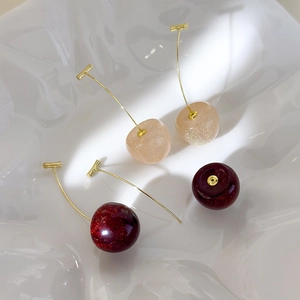 Detailed close-up of sparkling cherry earrings in pink and burgundy on a white tray