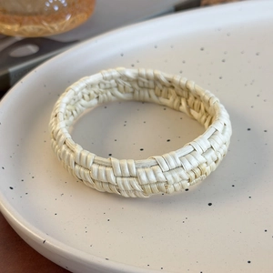 Vue détaillée du bracelet en rotin tressé ivoire sur un élégant plateau en céramique