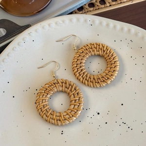 Detailed view of bohemian round woven rattan drop earrings with golden metal hooks