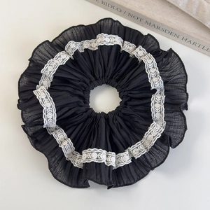 Detailed view of a black pleated scrunchie with white lace trim on a minimalist white backdrop