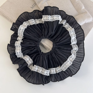 Close-up of oversized black scrunchie featuring white floral lace trim and pleated texture