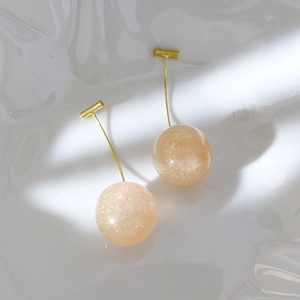 Close-up of pink glitter cherry resin earrings with golden hooks on white background
