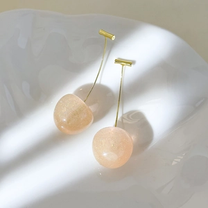 Detail of pink resin cherry earrings with golden glitter inside on a ceramic tray