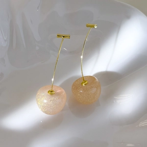 Macro detail of cherry-shaped resin earrings with shimmering glitter and gold hooks
