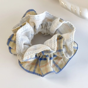 Detail of checkered plaid scrunchie with white lace trim in yellow and blue hues