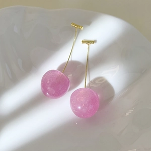 Macro detail of pink cherry resin earrings with fine glitter in a white ceramic tray