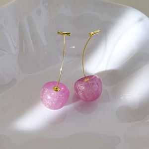 Macro shot of pink resin cherry earrings with glitter finish and elegant gold hooks