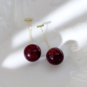 Detail view of cherry earrings with deep red glitter resin spheres and gold-plated metal stems