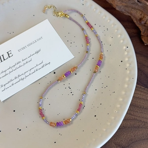 Détail du collier de perles fait main avec pierres violettes et oranges dans un bol