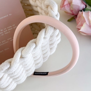 Detail of light pink satin headband with handmade label near white woven basket