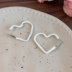 Macro view of cream white enamel heart earrings on a ceramic plate with warm lighting