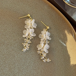 Detail of white matte floral earrings with crystal tassels on a ceramic tray