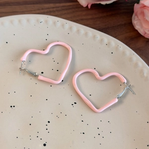 Detailed macro shot of pink heart-shaped enamel earrings on a ceramic dish with roses