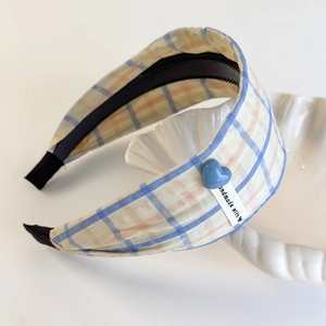 Close-up of plaid headband with blue heart charm and handmade tag on a shell tray