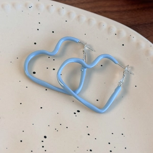 Macro detail of sky blue enamel heart hoop earrings on minimalist ceramic tray