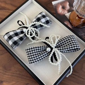 Detail of chic houndstooth bow hair clips with pearls and velvet on a beige display tray