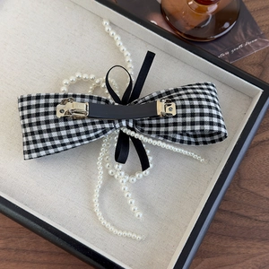 Detail of houndstooth bow hair clip featuring elegant faux pearl tassel and metal spring clip