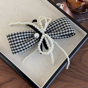 Close-up of elegant houndstooth ribbon hair clip with pearl bow detail and velvet texture