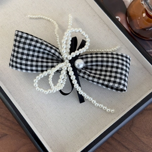 Detailed view of houndstooth bow hair clip with white pearls and black velvet texture