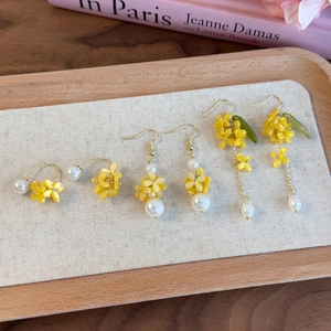 Dettaglio di orecchini a fiore giallo con perle e nappe su un vassoio di legno per gioielli