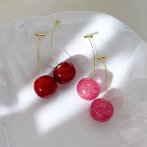 Sparkling cherry dangle earrings in red and pink colors with gold hooks on white plate