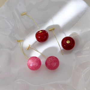 Close-up of glittery cherry earrings in red and pink on white ceramic tray