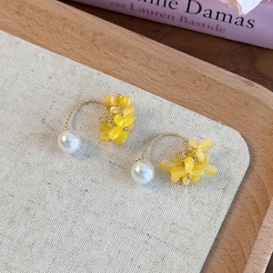 Dettaglio di orecchini a fiore dorati con perle e nappe su un vassoio di legno