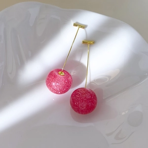 Macro shot of pink cherry earrings with silver glitter on white ceramic tray