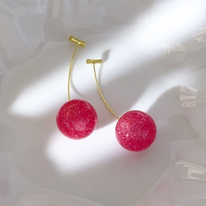 Detailed top view of cherry earrings with pink glitter beads on white wavy tray