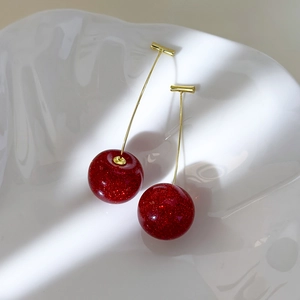 Detailed macro view of cherry-shaped long earrings with red glitter resin on a white plate