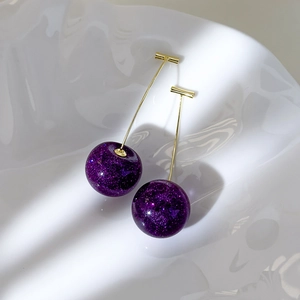 Detailed macro view of purple cherry earrings with glitter resin and golden metal stems