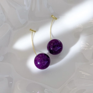 Detail of purple cherry earrings with glitter finish and golden stems on white texture