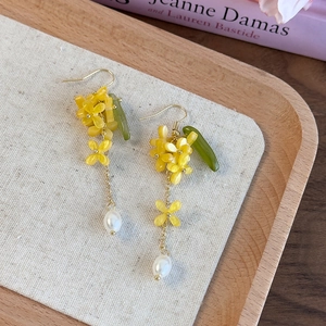 Dettaglio di orecchini floreali con petali gialli, foglia verde e nappe di perle su lino