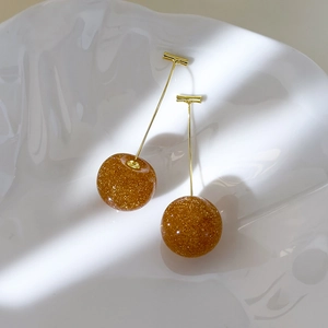Detail of amber cherry earrings with gold sparkles on a stylish white ceramic tray