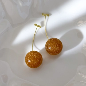 Detail of cherry-shaped gold glitter resin earrings with gold-toned metal stems