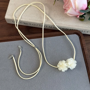 Détail d'un choker en daim beige avec fleurs de camélia blanches sur un bureau en bois