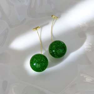 Macro view of cherry-shaped earrings with green glitter globes on a ceramic plate