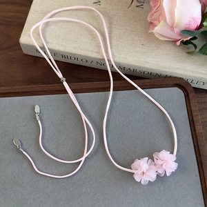 Gros plan d'un collier choker fleur de camélia rose sur un plateau en bois gris