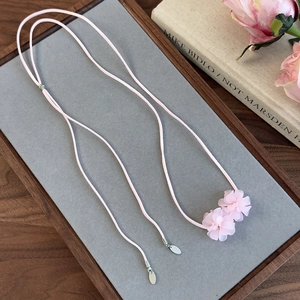 Détail des pendentifs camélia rose sur un long collier en corde de daim souple