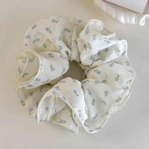 Detailed view of white floral scrunchie with blue daisy pattern on soft textured fabric