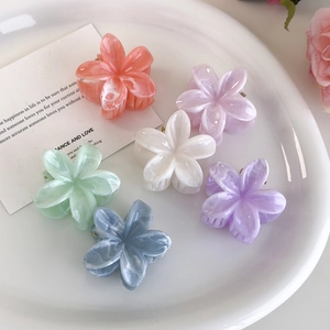 Set of six marble-textured plumeria hair claws in pastel colors displayed on a white plate
