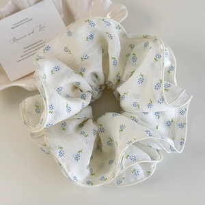 Close-up of white pleated floral scrunchie with blue flower pattern on a shell tray
