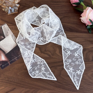 Close-up of white floral lace scarf with embroidered logo detail on dark wood surface