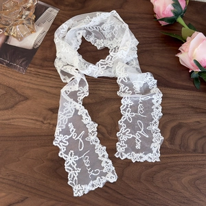 Close-up of white lace scarf with letter embroidery and floral patterns on wood surface