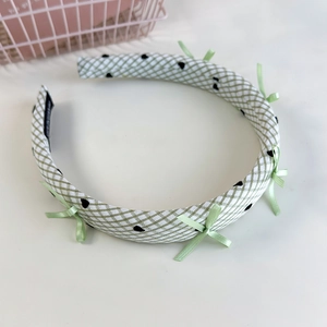 Détail du serre-tête à carreaux verts avec cœurs noirs et nœuds sur fond blanc